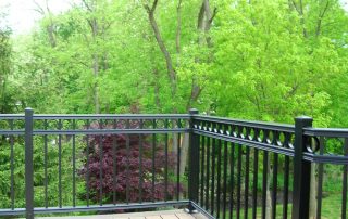 fancy black railing for a brown deck with lush trees in the background