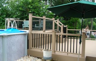 tan patio/deck area with black railings leading to an above ground pool